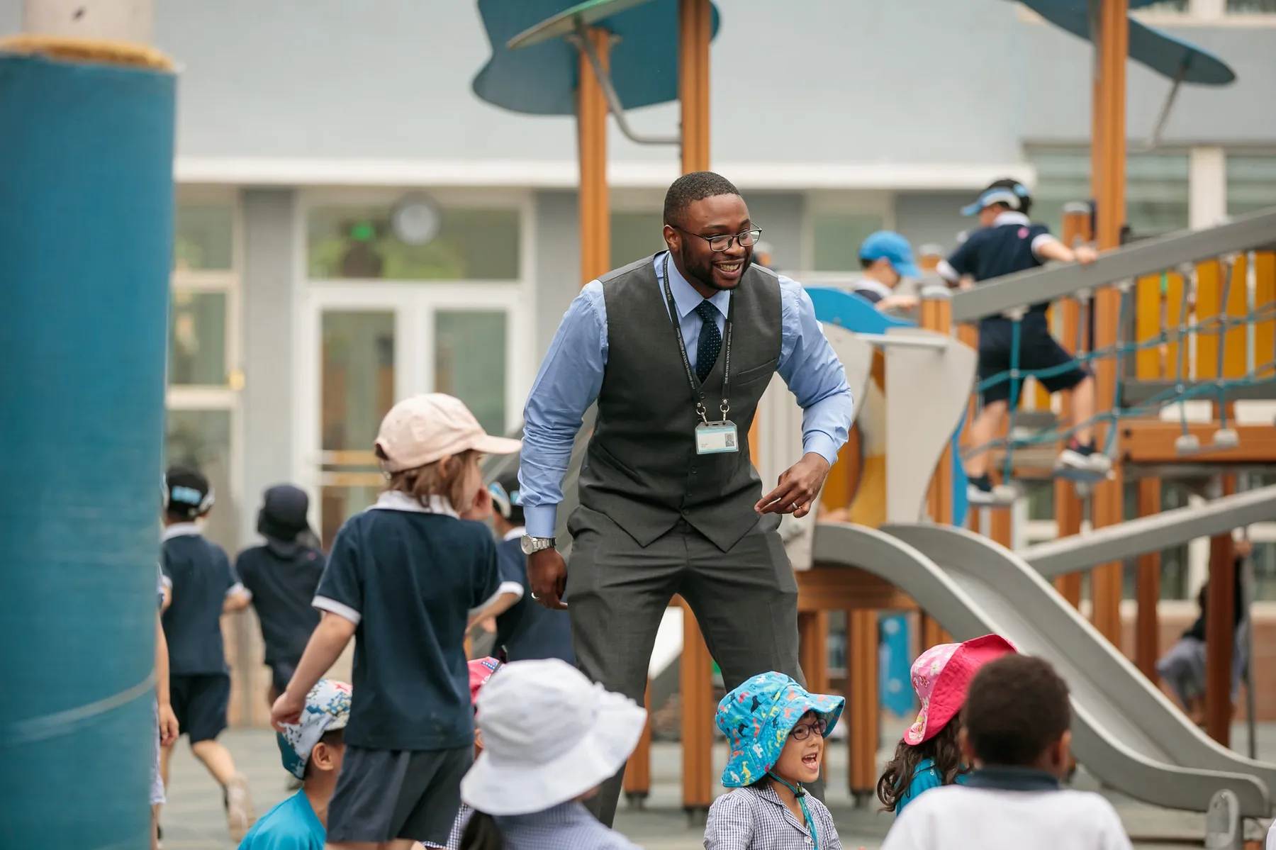 A teacher plays with laughing young pupils in the school playground