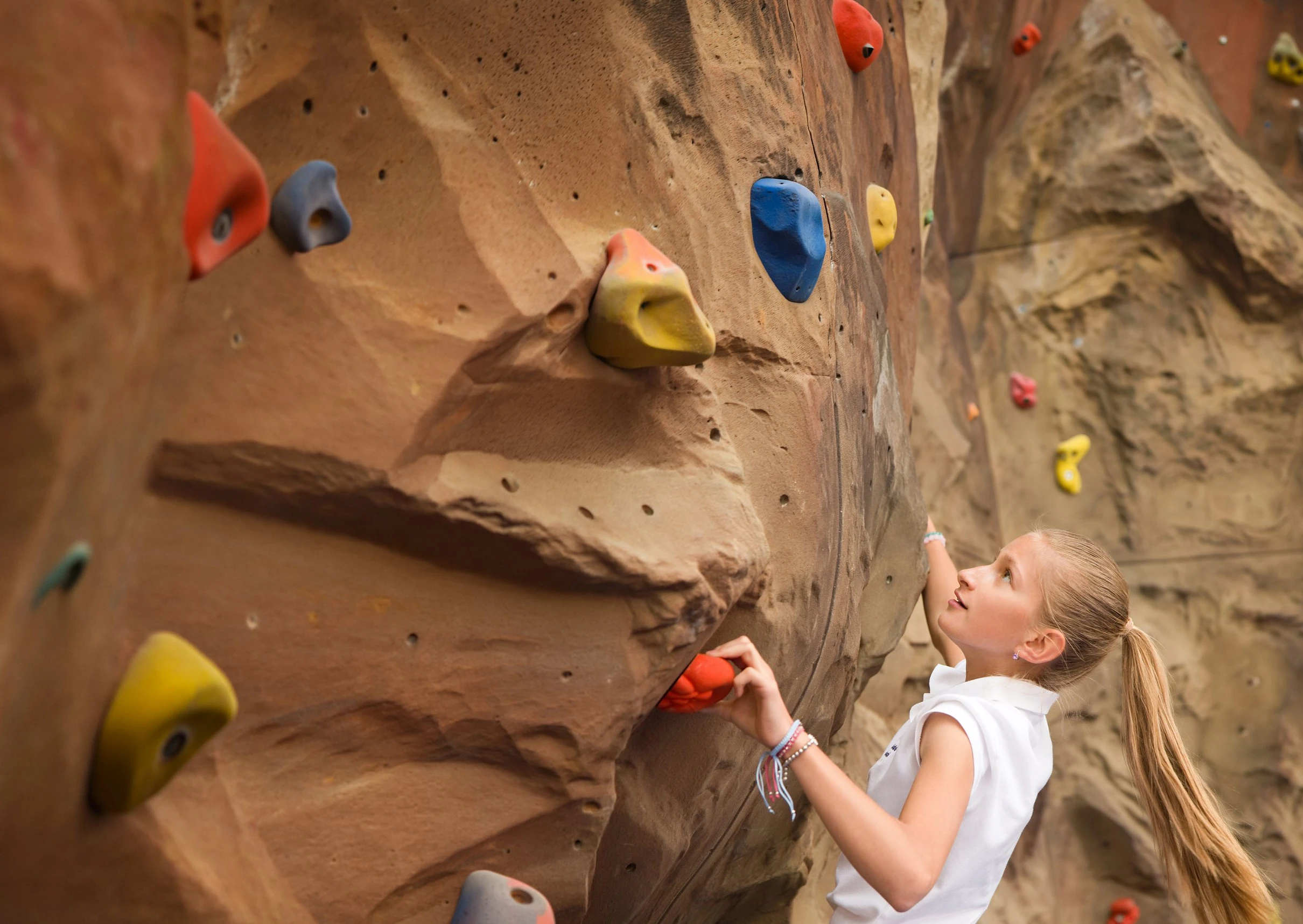 A student on the school climbing wall, reaching for the next hold and looking up to plan her route